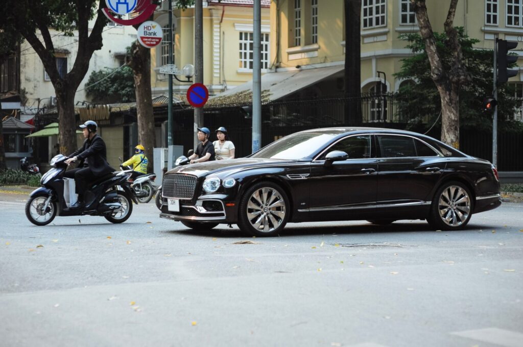 A luxury car and motorbikes wait at a city intersection, capturing urban street life.