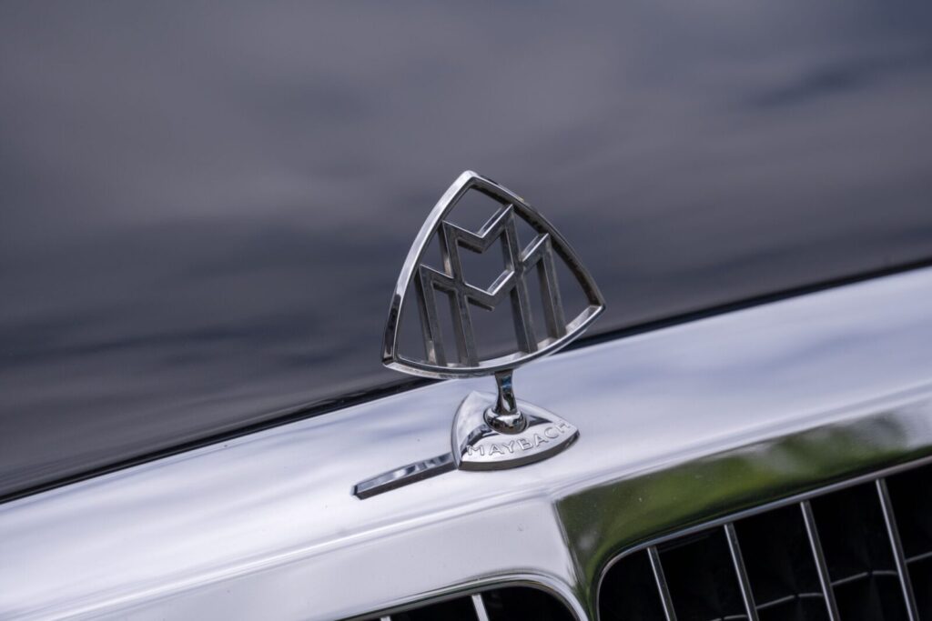 Close-up view of the Maybach car emblem on a shiny hood, reflecting a luxury vehicle's elegance.